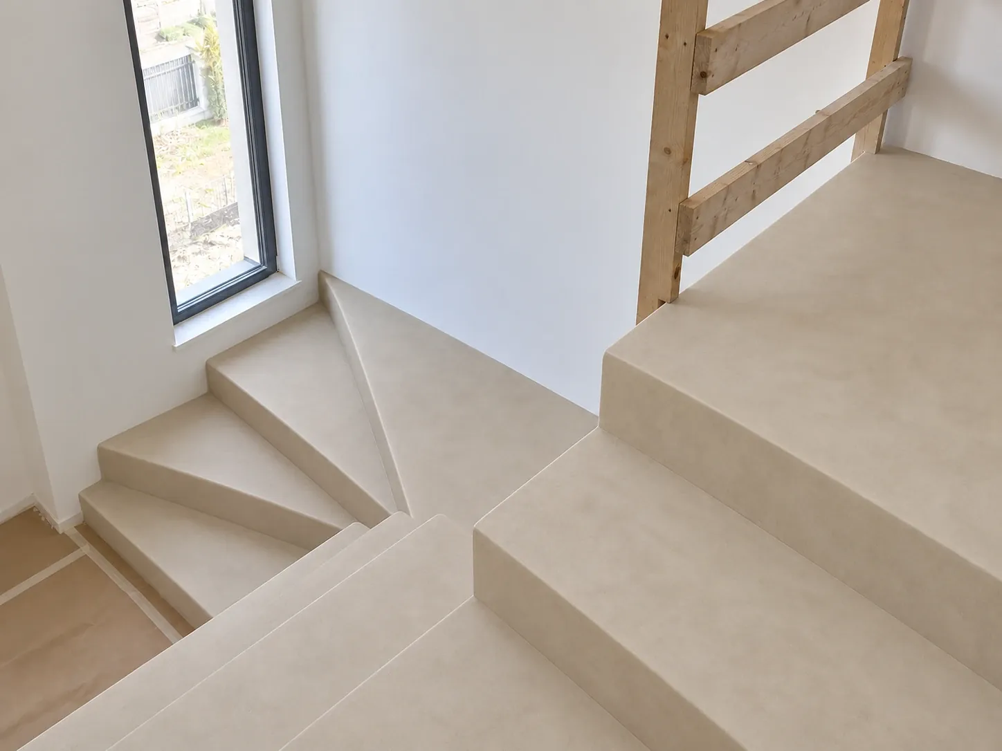 Schody zabiegowe z beżowego mikrocementu, widok z góry na stopnie i podest